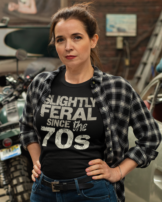 Woman wearing a black t-shirt with 'Slightly Feral Since the 70s' text, standing in a garage.