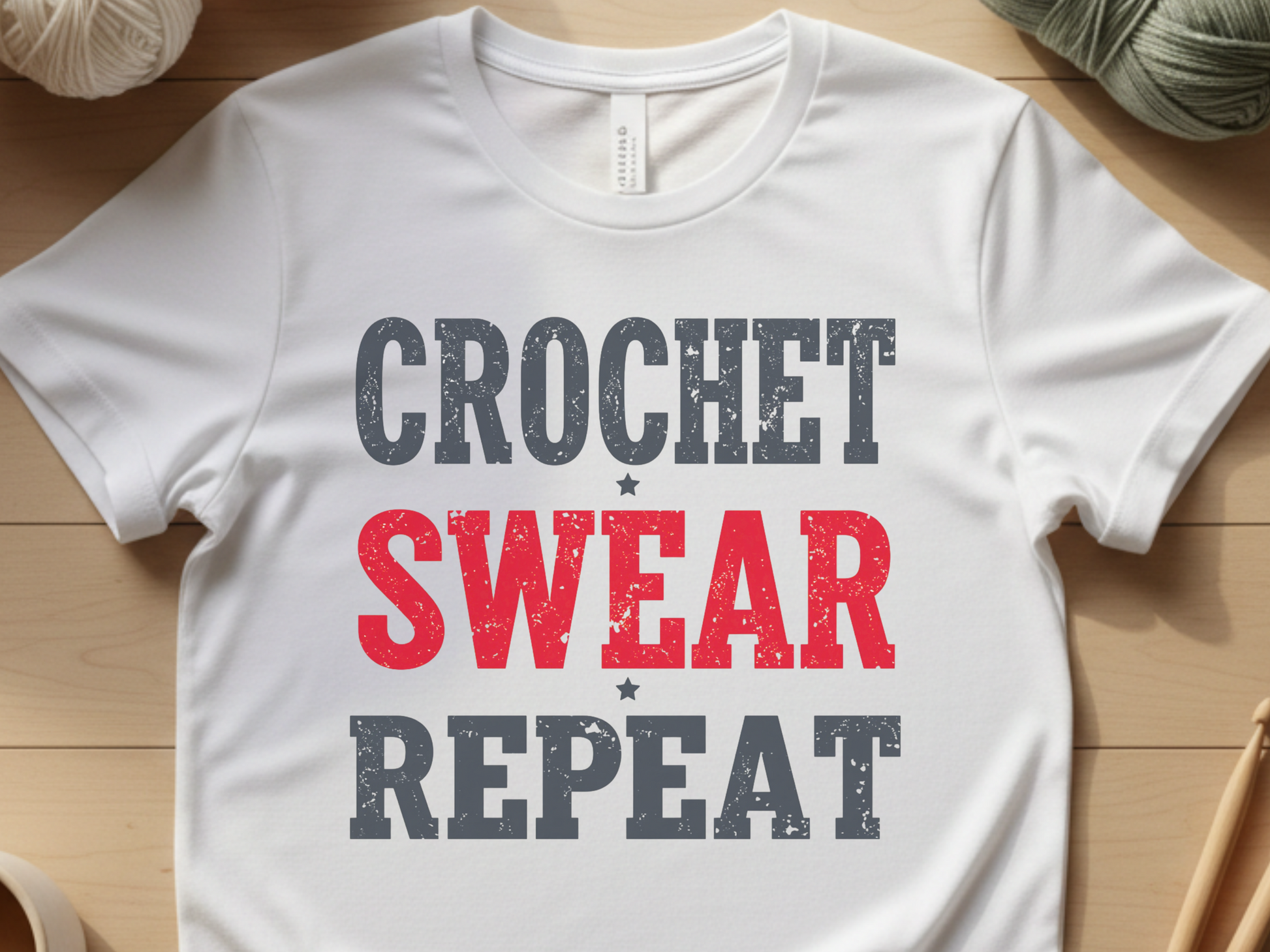 White t-shirt with 'Crochet Swear Repeat' text on a wooden surface with yarn and crochet hooks.