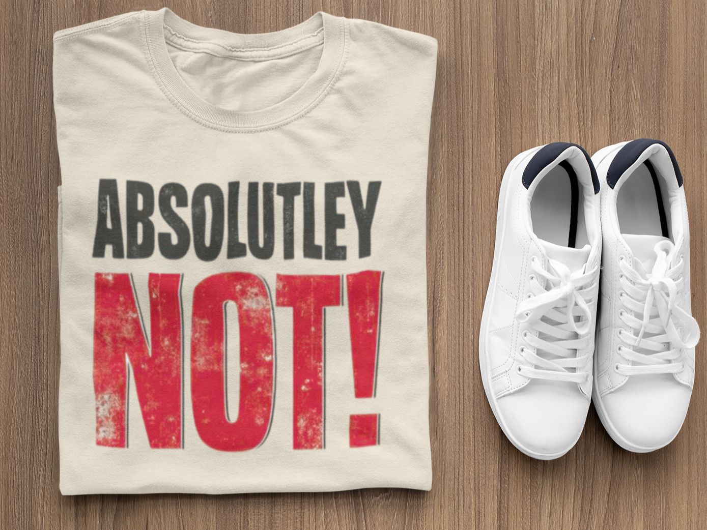 Beige t-shirt with 'ABSOLUTLEY NOT!' text and white sneakers on a wooden surface