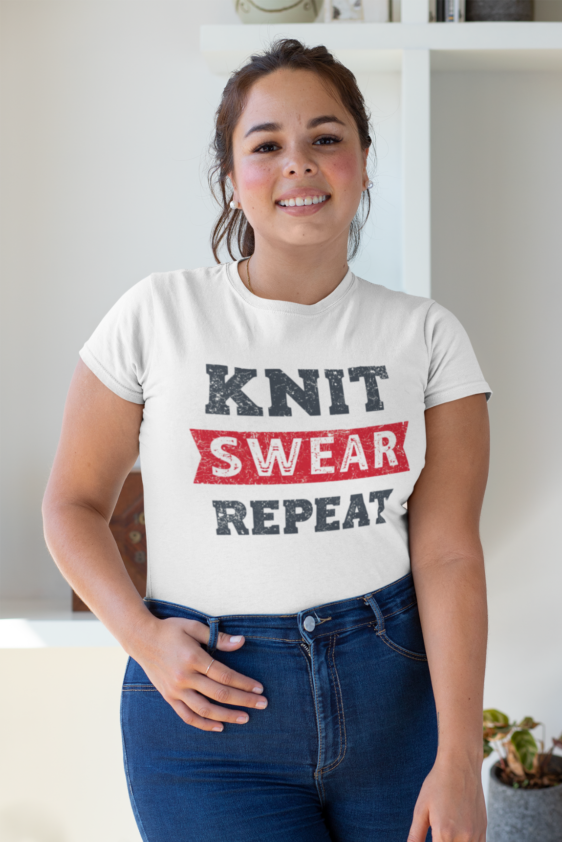 Person wearing a white t-shirt with 'KNIT SWEAR REPEAT' text in a casual setting.