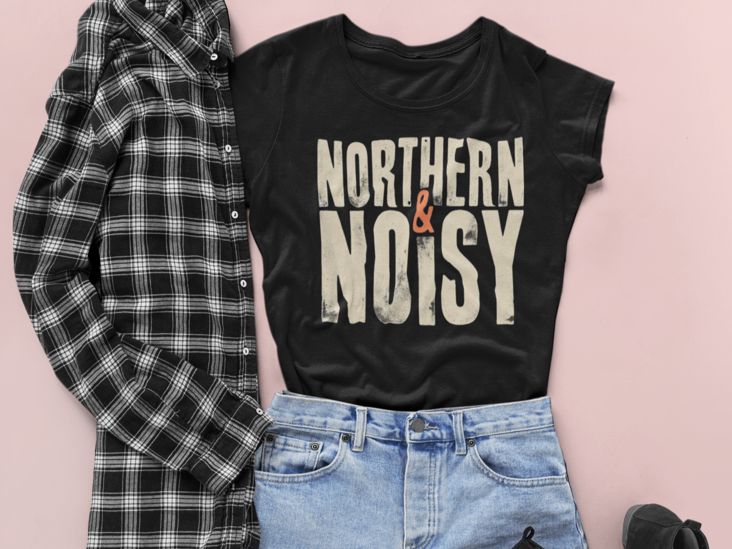 Black t-shirt with 'Northern & Noisy' text, plaid shirt, and jeans on a pink background