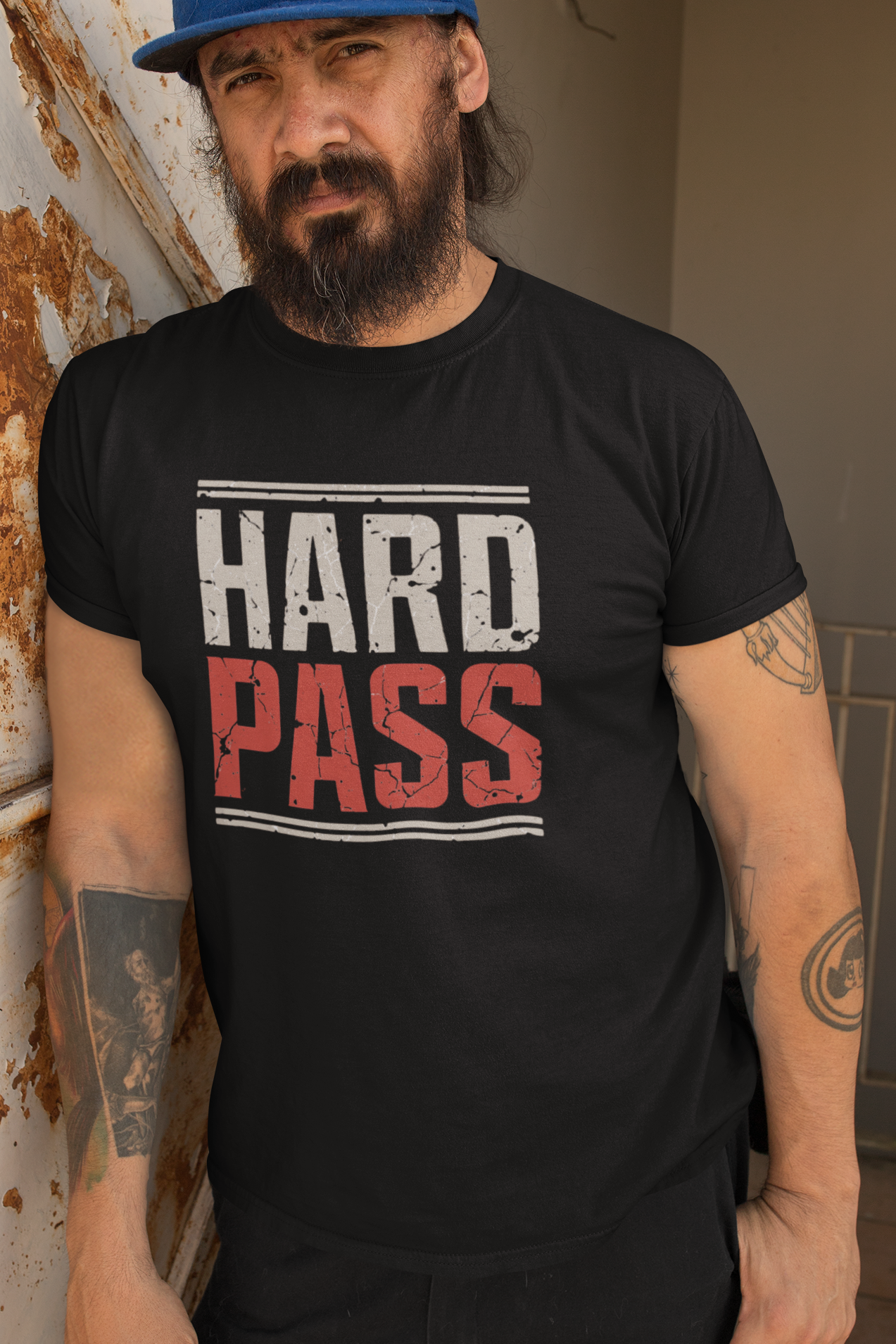 Man wearing a black t-shirt with 'HARD PASS' text, standing against a rustic wall.