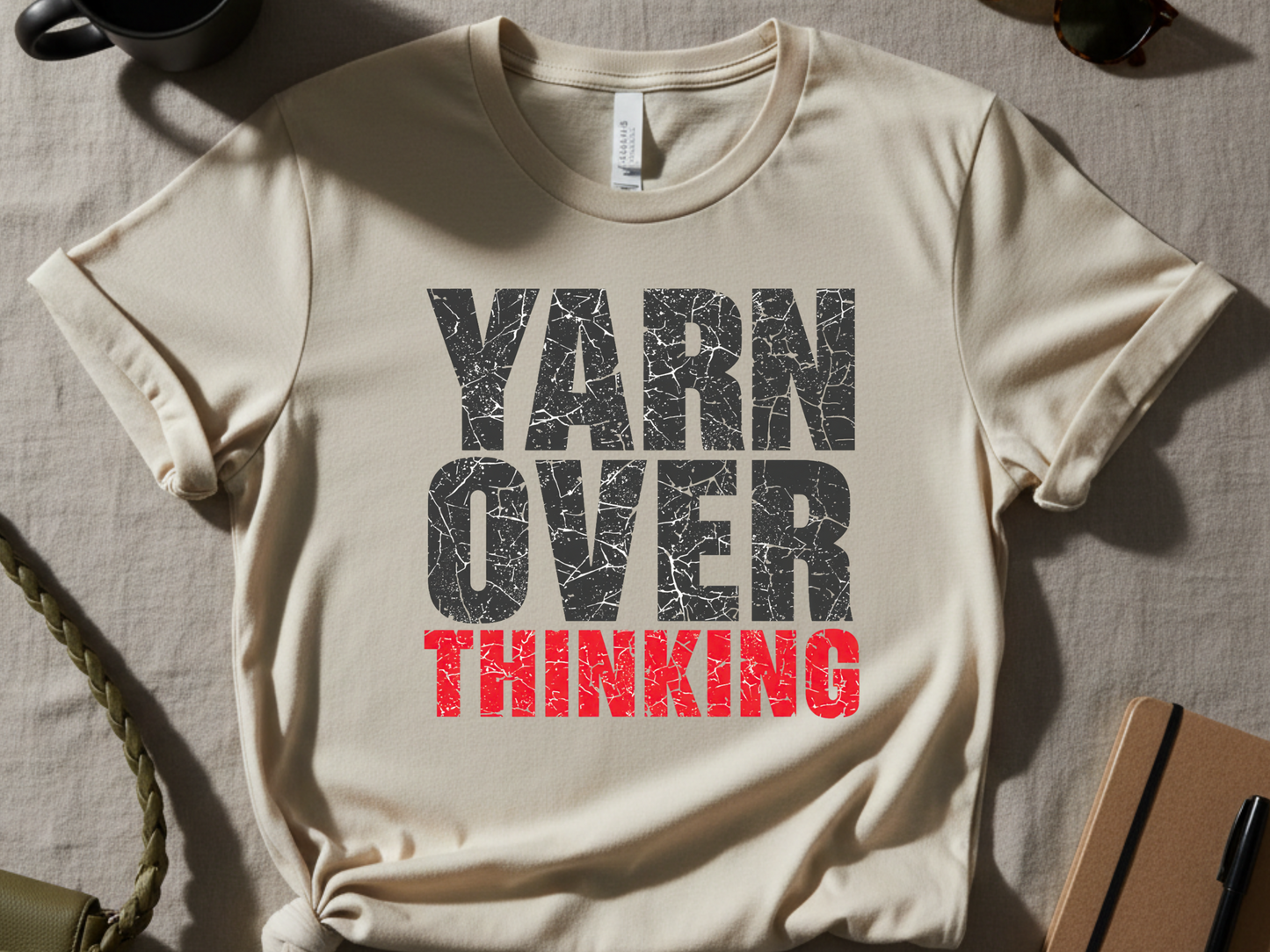 Beige t-shirt with 'YARN OVER THINKING' text on a textured surface