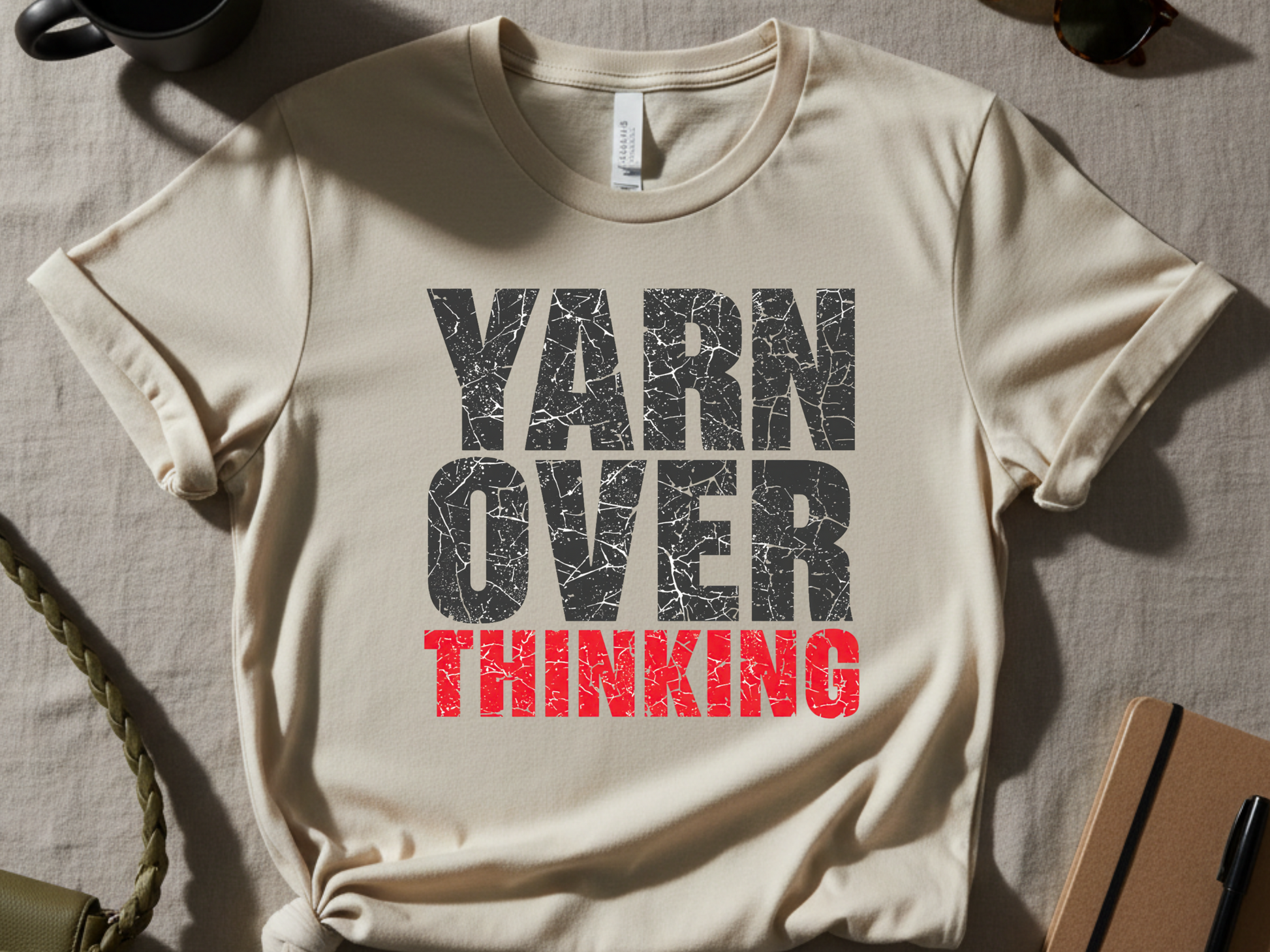 Beige t-shirt with 'YARN OVER THINKING' text on a textured surface