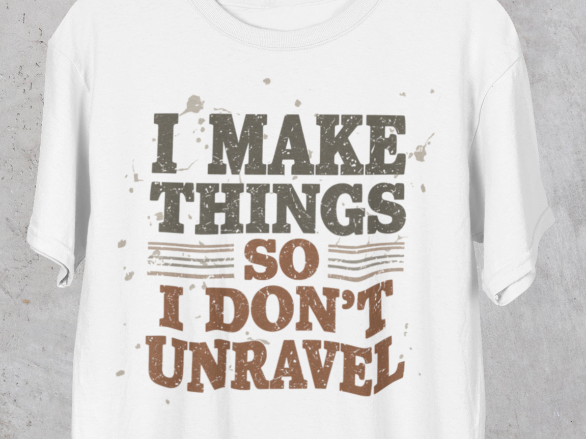 White t-shirt with text 'I MAKE THINGS SO I DON'T UNRAVEL' on a gray background