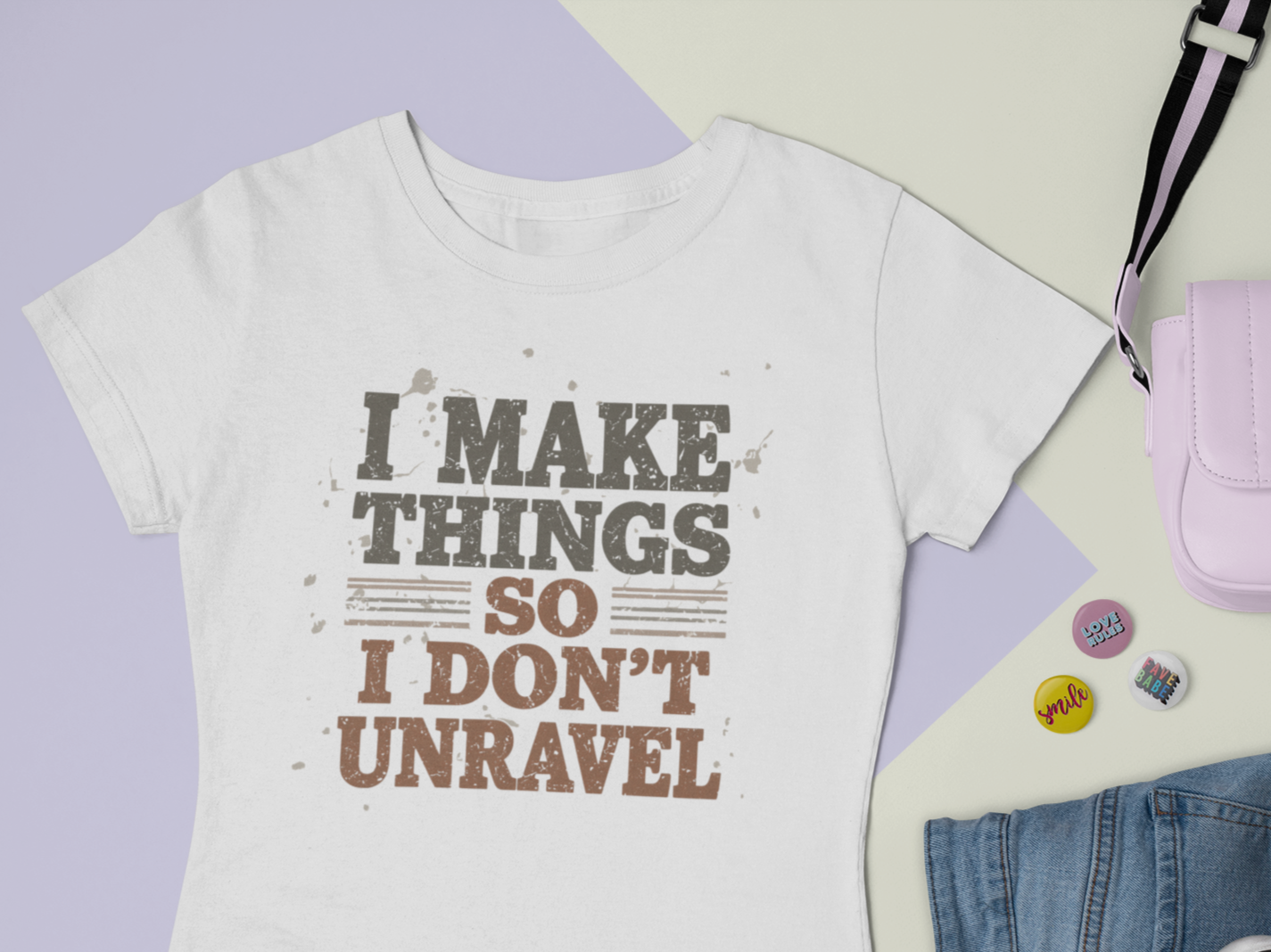 White t-shirt with 'I make things so I don't unravel' text, purple pouch, and denim jeans on a light purple background